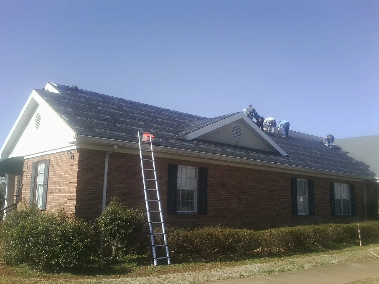 Crew tearing shingles off a brick ranch roof with a ladder set — Emergency Roof Repair work by our crew in Aliso Viejo