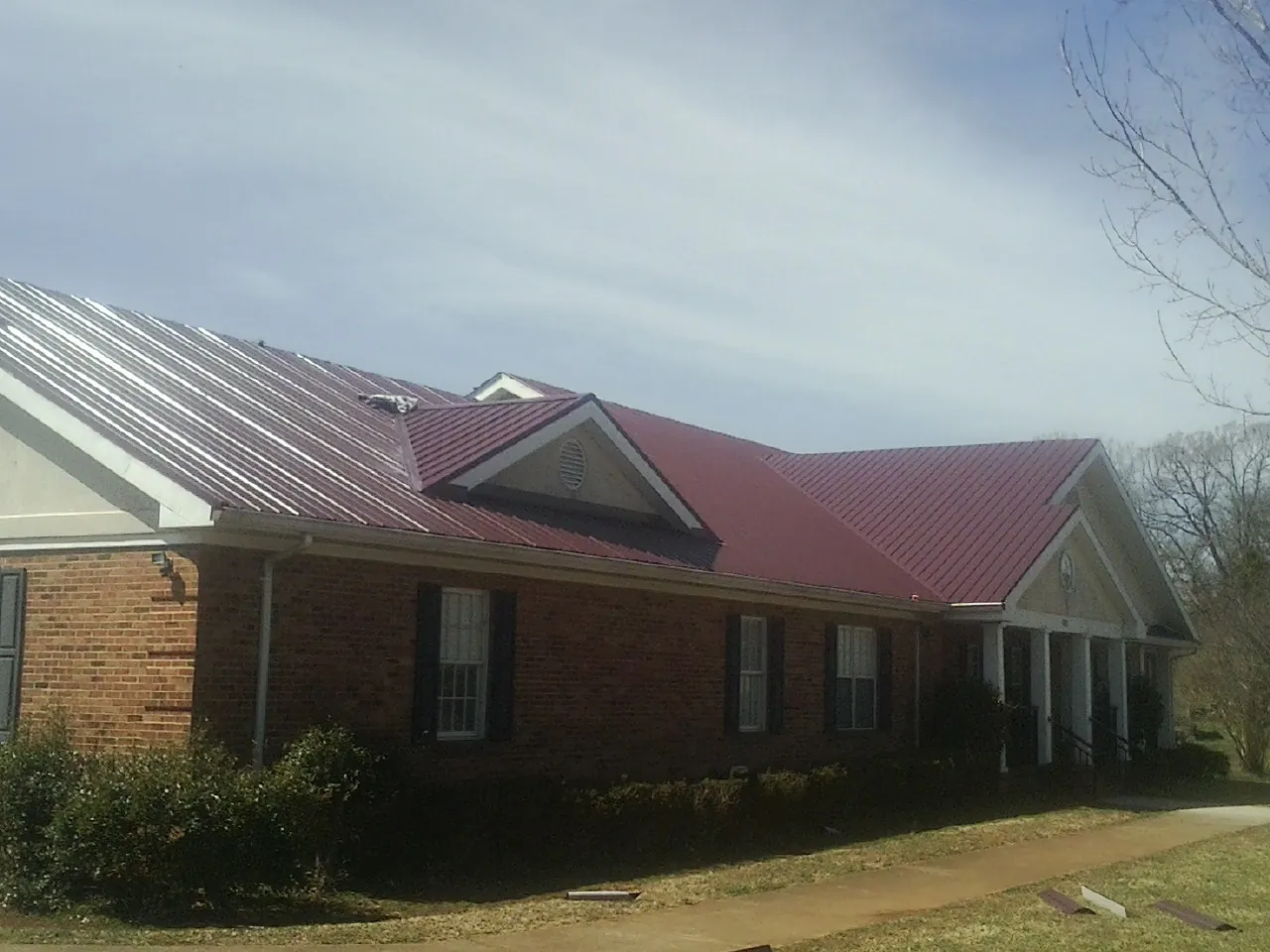 Red metal roof with gabled entries on a long brick building, from a Hail Damage Roof Repair job in Aliso Viejo