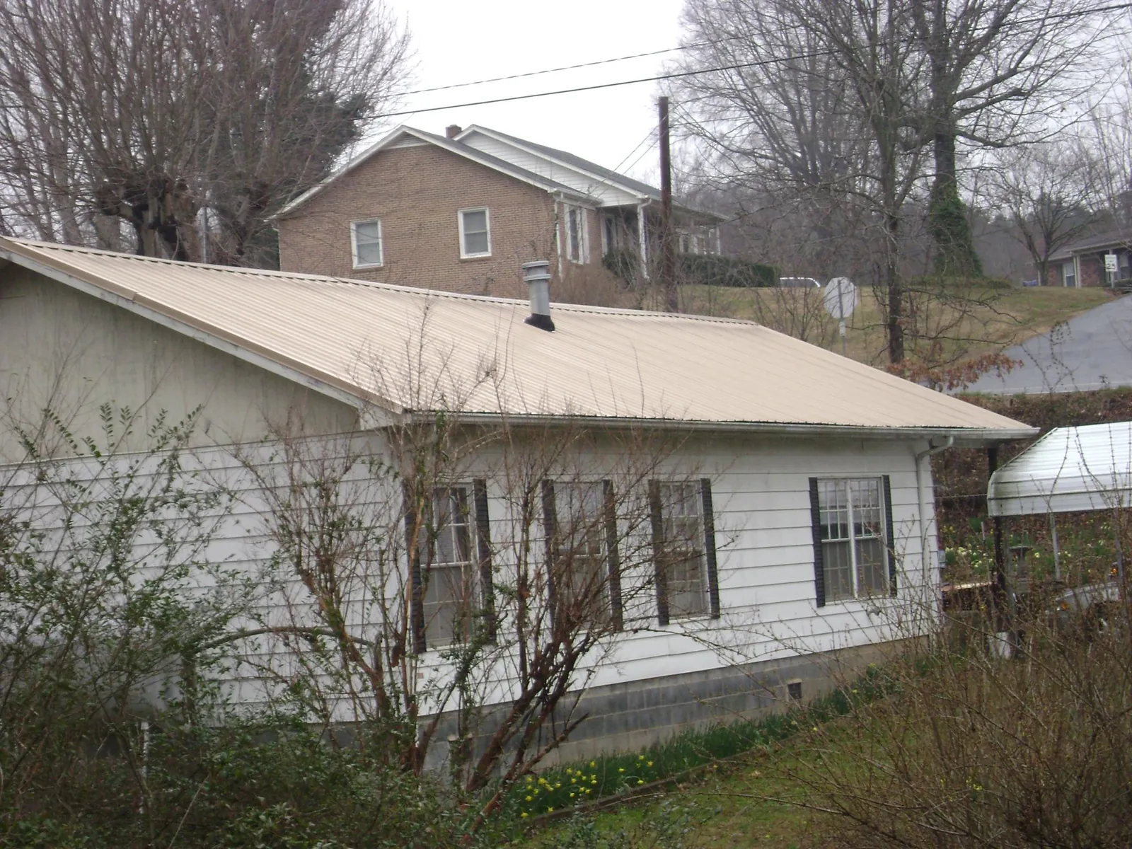 Tan metal roof on a white sided house set into a hillside — Commercial Roofing by Roofing Brothers in Aliso Viejo